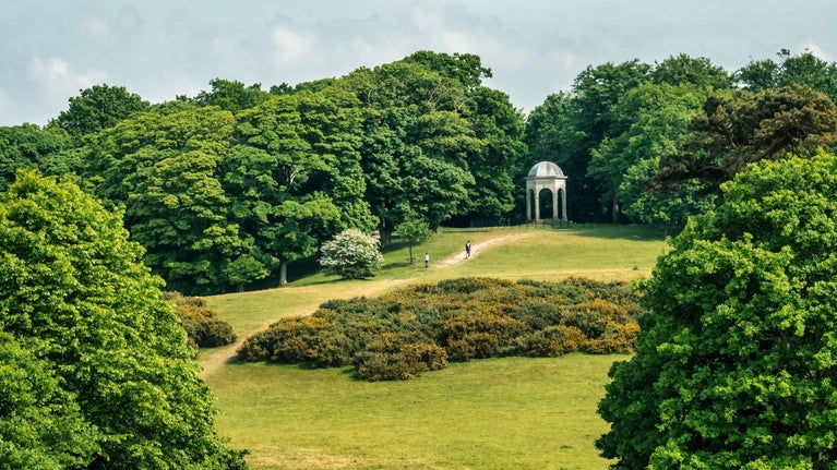 Two people walking up a hill on a summer's day towards the Temple at Sheringham Park.